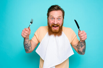 Hungry man with tattoos is ready to eat with cutlery in hand