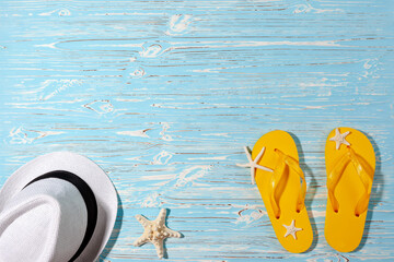 yellow rubber flip flops, white beach hat, starfish on a blue wooden background