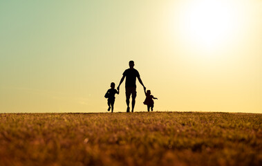 Father and his children walking together holding hands in the park. Fathers Day, family, and parenting concept.  - obrazy, fototapety, plakaty