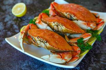 Three boiled crabs with lemon and parsley on a white plate.