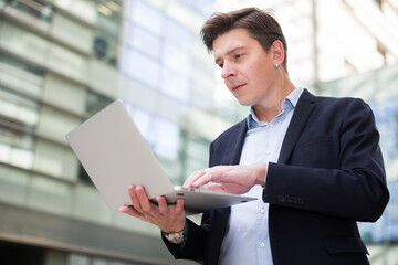 Cheerful businessman with notebook talking about work on the mobile phone at the street