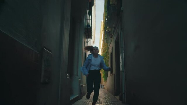 Incredible action low angle shot of young woman run through narrow city street of european town. She looks at phone, to check time of appointment. Scared and nervous, running late for meeting