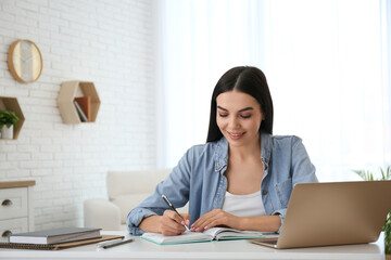 Young woman taking notes during online webinar at table indoors