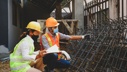 Fototapeta premium Asian construction engineers inspecting reinforced steel bars and reviewing building plans at construction site wearing safety helmets and reflective vests