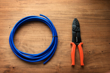 Cable or wire and a wire cutter or crimping pliers on a wooden work desk.