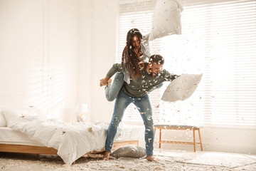 Happy young couple having fun pillow fight in bedroom