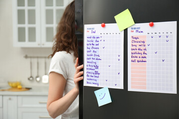 Fototapeta na wymiar Woman near refrigerator with to do lists on door in kitchen