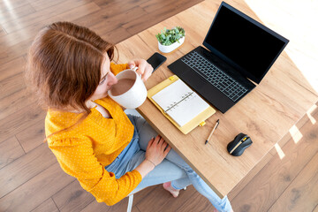 Defocus. Young business woman is resting with a cup of cocoa after work Internet using a computer.