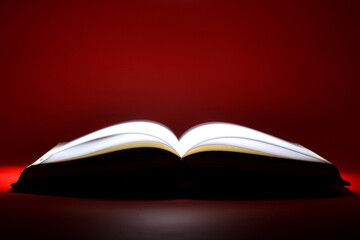 A book that looks like a Bible open in dark and red color background with very bright golden light...