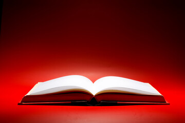 A book that looks like a Bible open in dark and red color background with very bright golden light on the page. Spiritual Life concept.