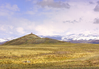Kurai steppe in spring. Viewing gazebo on a hilltop in the middle of dry grass, snow-capped peaks...