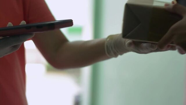 Close up of girl's hand receive a parcel from a delivery woman and using QR code scan with smartphone for payment. Scanning and paying on mobile device. Delivery to home concept.