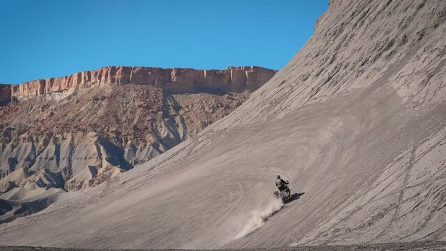 Motorcycle rider climbs hill in Utah. Offroad stuntman riding motorbike up a sand mountain in slow motion on a road trip on a adventure motorbike Yamaha Tenere 700 T7.