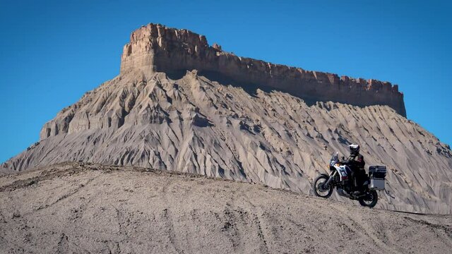 Motorcycle rider on Yamaha Tenere Adventure Bike driving up to cliff overlooking scenic outlook with alien mountain in background in 180 fps slow motion.