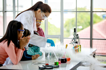 Group of Asian elementary little boy and girls wear safety goggles excited and looking at smoke reaction in school lab in science subject education hour