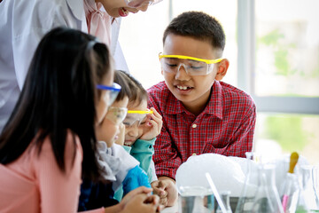 Asian female elementary school science teacher in lab coat holding colorful laboratory equipment in...