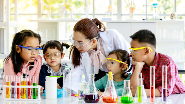 Asian female professional scientist teacher in white lab coat rubber gloves and safety glasses teach science experiment to primary schoolboy and schoolgirls in laboratory with test tubes microscope