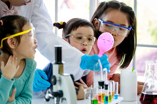 Closeup shot group of Asian little curious elementary schoolgirls wears safety goggles looking observing at water bottle reaction blowing pink rubber balloon experiment teach by science teacher