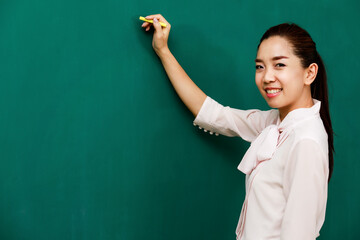 Portrait closeup shot of Asian young female beautiful school teacher tutor professor lecturer standing smiling holding chalk in hand writing on chalkboard while teaching student in university campus