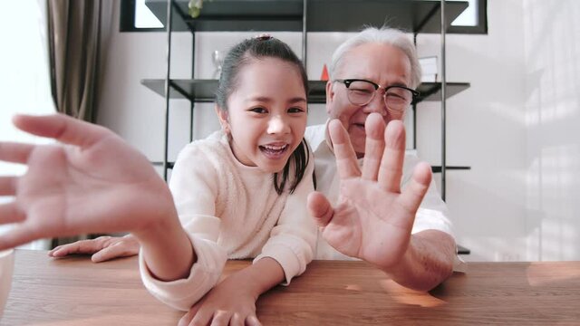 Senior Asian man and granddaughter talking via video call with family members.