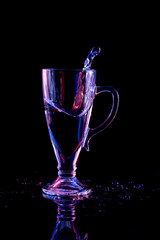 Still life with a glass beaker with splashed liquid on a black background