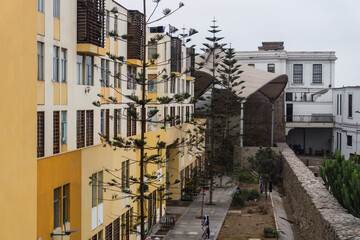 Aged facade of modern multi - storey  colored residential building in historic center of Lima Peru, yellow and orange walls, trees.