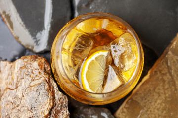 Glass of whiskey with lemon and ice on stone background.