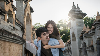 Happy Asian couple traveler, Romantic female riding on back of boyfriend smile in love and travel...