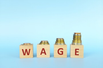 Salary or wage increase concept. Increasing stack of coins on wooden blocks in blue background.