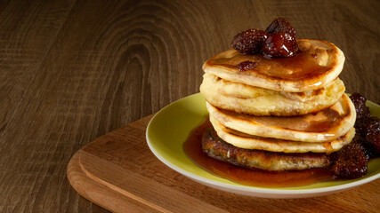 Several pancakes with strawberry jam and berries on a wooden board