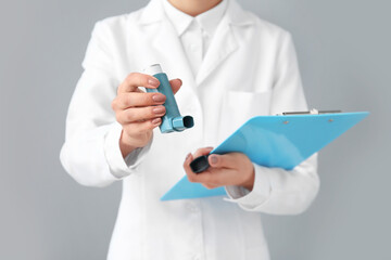 Female allergist with inhaler and clipboard on grey background