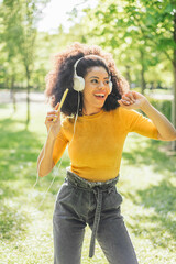 Pretty afro woman listens to music with headphones in a garden.