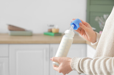 Woman with bottle of milk for baby in kitchen