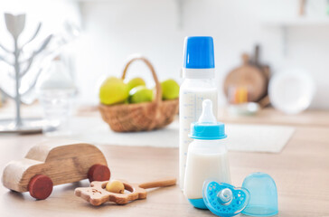 Bottles of milk for baby with toys on table in kitchen