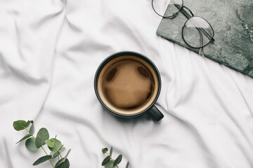 Cup of coffee and glasses on bed
