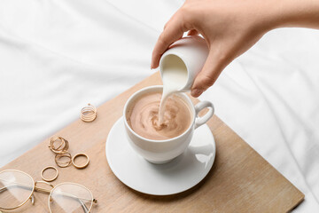 Woman pouring milk into coffee on bed
