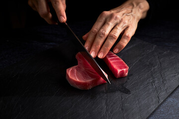 Female cook preparing a piece of bluefin tuna to make sushi. Asian food concept - obrazy, fototapety, plakaty