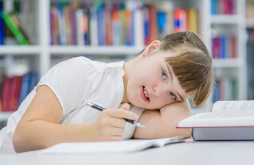 Tired young girl with syndrome down doing homework at library. Education for disabled children concept