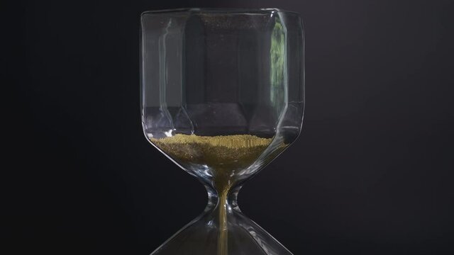 4K video Close up of falling sand in sand clock on black background. Concept for running time and time in motion.