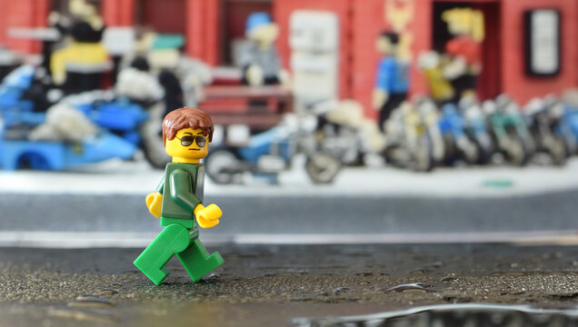 Lego minifigure in green is walking down a street. Editorial illustrative image of lego city.