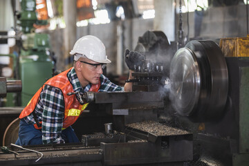 worker is working on a lathe machine in a factory. Turner worker manages the metalworking process of mechanical cutting on a lathe - obrazy, fototapety, plakaty