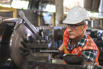 worker is working on a lathe machine in a factory. Turner worker manages the metalworking process of mechanical cutting on a lathe