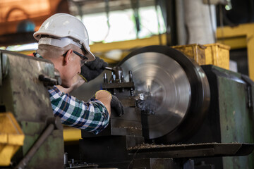 worker is working on a lathe machine in a factory. Turner worker manages the metalworking process...