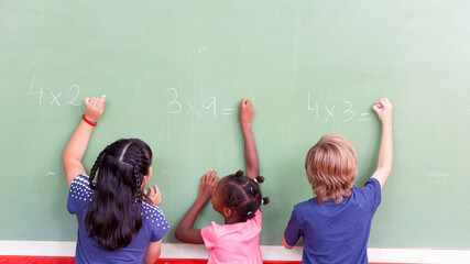 Mixed race school children writing on chalkboard