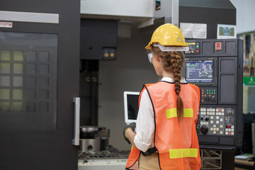 Factory worker is programming a CNC milling machine with a tablet computer. engineering and worker woman in safety hard hat and reflective cloth using lathe machine inside the factory.