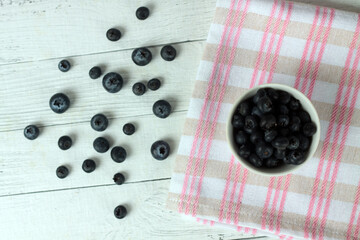 a bowl of blueberry and berries on a napkin on wooden background flat lay