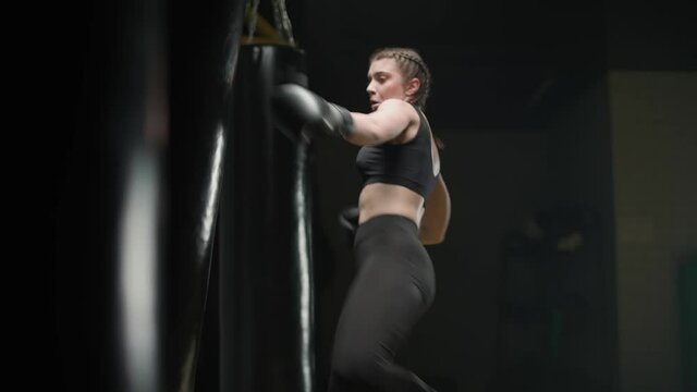 Female fighter trains his punches, beats a punching bag, kickboxing training day in the boxing gym, 4k slow motion.