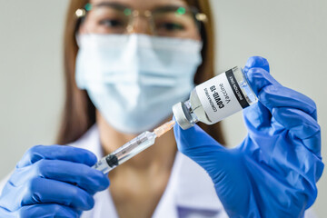 Coronavirus (COVID-19) vaccine and syringe carried by blue gloved medical professionals.