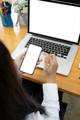 Rear view of young woman sitting in front of laptop computer and using mobile phone.
