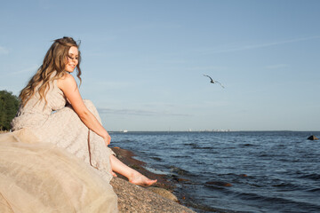 Fototapeta na wymiar Beautiful woman in fashionable romantic lacy dress sitting by the sea